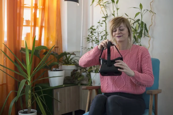 woman in pink sweater at home enjoying using virtual reality goggles in modern armchair Looking around and using gestures with hands