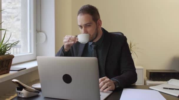 古賀ウィンドウ黒テーブルのノート ペーパー電話社長とオフィスでラップトップのコーヒー作業を飲むビジネスマン — ストック動画
