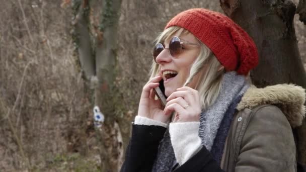 携帯電話で話す木のそばに座って赤い帽子と言えば若い魅力的な女性のモバイル Phoneportrait の木のそばに座って赤い帽子と若い魅力的な女性 冬の公園で座っている女性 — ストック動画