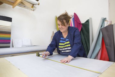 Yaşlı kadın bir mobilya fabrikasında ölçme ve işaretleme bir takoz ile kanepe için gri bir malzeme