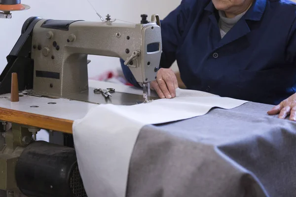 Closeup of an older woman in a furniture factory who is sewing the material for the sofa