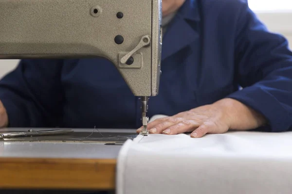 Closeup of an older woman in a furniture factory who is sewing the material for the sofa