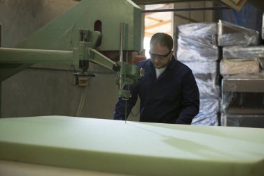 Genç adam bir mobilya fabrikasında kanepe için köpük kesme