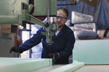 Genç adam bir mobilya fabrikasında kanepe için köpük kesme