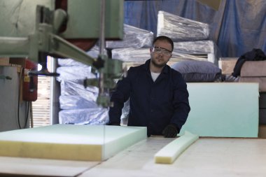 Genç adam bir mobilya fabrikasında kanepe için köpük kesme