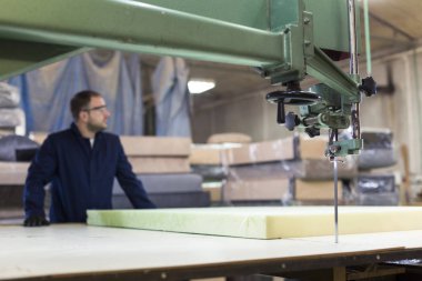 Genç adam bir mobilya fabrikasında kanepe için köpük kesme