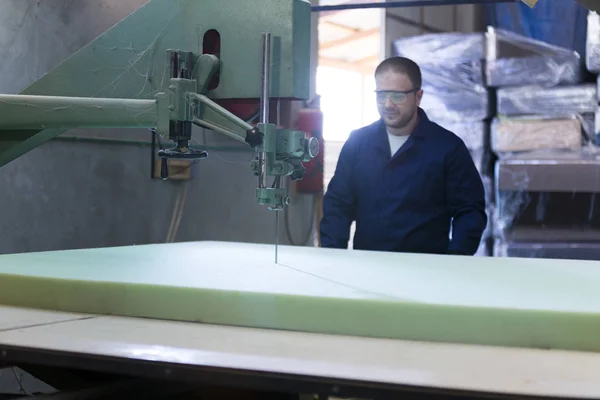 Young man in a furniture factory is cutting the foam for the sofa