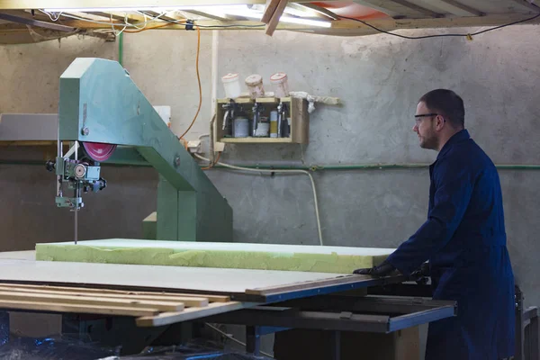 Молодой человек на мебельной фабрике режет пену для дивана — стоковое фото