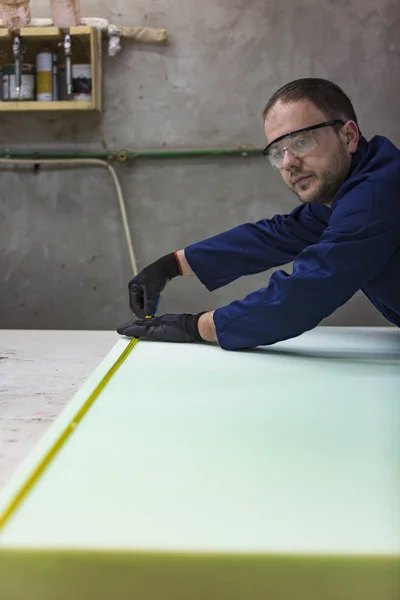 Молодой человек на мебельной фабрике измеряет пену для дивана . — стоковое фото