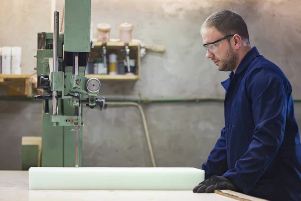 Portrét mladého muže v továrně na nábytek, řezání pěny na pohovce — Stock fotografie