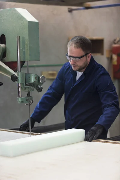 Portrait of a young man in a furniture factory cutting the foam for the sofa