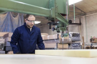 Genç adam bir mobilya fabrikasında kanepe için köpük kesme