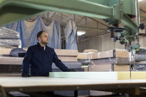 Young man in a furniture factory is cutting the foam for the sofa