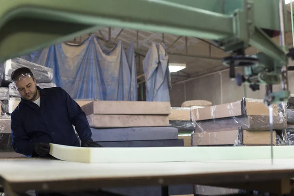 Молодой человек на мебельной фабрике режет пену для дивана — стоковое фото