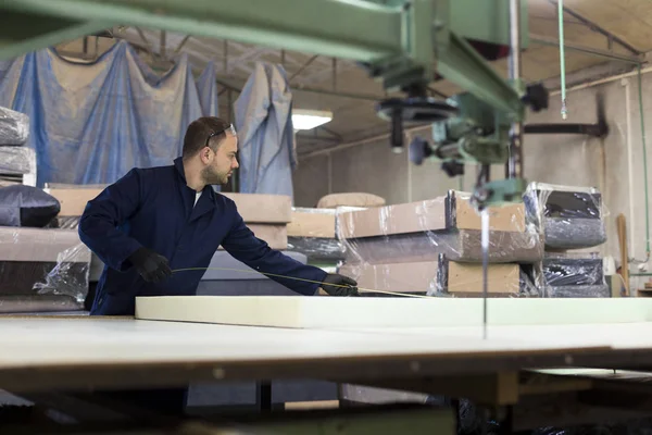 Young man in a furniture factory is measuring the foam for the sofa.