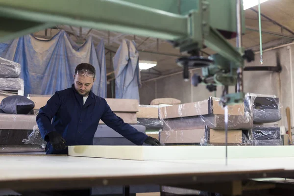 Young man in a furniture factory is measuring the foam for the sofa.