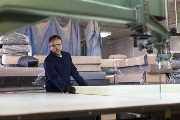 Young man in a furniture factory is cutting the foam for the sofa