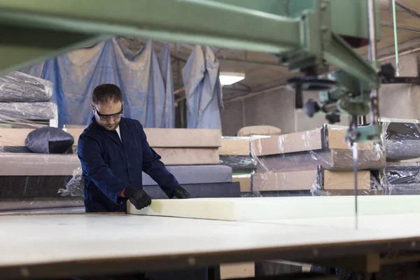 Giovane in una fabbrica di mobili sta tagliando la schiuma per il divano — Foto Stock