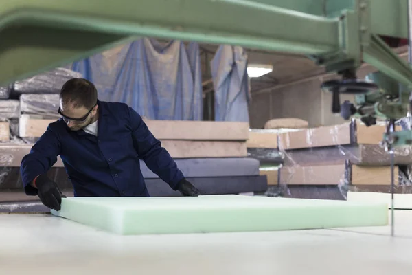 Young man in a furniture factory is cutting the foam for the sofa