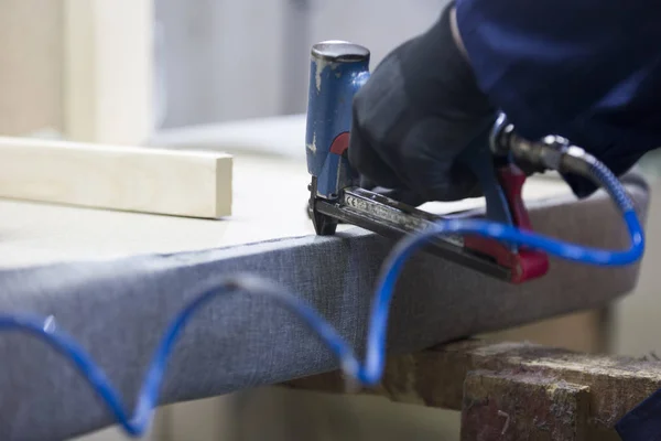 Closeup of a young man in a furniture factory who puts together one part of the sofa with a stapler