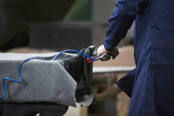 Closeup of a young man in a furniture factory who puts together one part of the sofa with a stapler