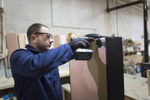 Young man in a furniture factory attaches the sofa leg