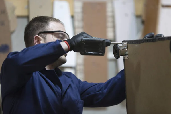 Young man in a furniture factory attaches the sofa leg