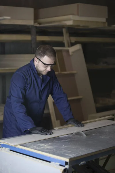 Молодой человек на мебельной фабрике режет деревянные детали для дивана — стоковое фото