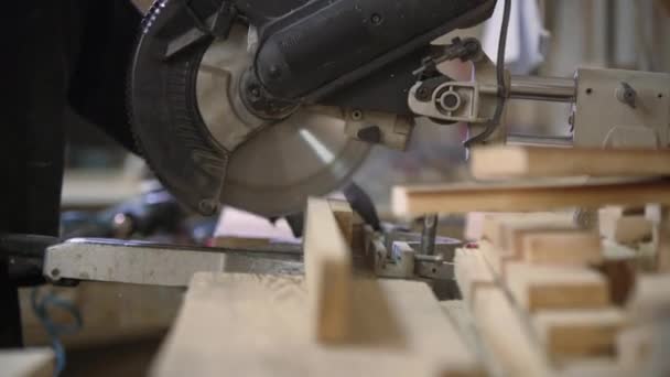 在一家家具厂的一个年轻人附近剪掉木片作为沙发 家具生产过程 一个穿着深色外套的年轻人在切割机上为沙发剪断了木片 他戴着安全眼镜和手套 — 图库视频影像