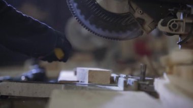 Bir gencin kanepede için ahşap parçalar kesilmesi bir mobilya fabrikasında kapatın. Mobilya üretim süreci. Genç ceket bir adam, bir karanlık kanepe için ahşap parçalar üzerinde kesme makinesi kesin. Koruyucu gözlük takıyor ve eldiven.