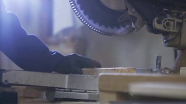 Bir gencin kanepede için ahşap parçalar kesilmesi bir mobilya fabrikasında kapatın. Mobilya üretim süreci. Genç ceket bir adam, bir karanlık kanepe için ahşap parçalar üzerinde kesme makinesi kesin. Koruyucu gözlük takıyor ve eldiven.