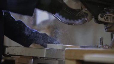 Bir gencin kanepede için ahşap parçalar kesilmesi bir mobilya fabrikasında kapatın. Mobilya üretim süreci. Genç ceket bir adam, bir karanlık kanepe için ahşap parçalar üzerinde kesme makinesi kesin. Koruyucu gözlük takıyor ve eldiven.