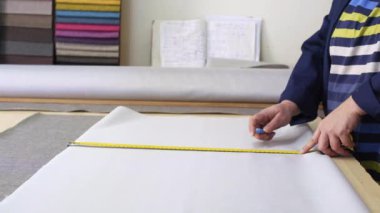 Karanlık bir kat büyük bir kadında ölçer ve gri malzeme kanepe için işaretler. Arkasındaki kadın malzemeleri farklı türleri vardır. O ölçme ve işaretleme malzeme kesim için hazırlanıyor.