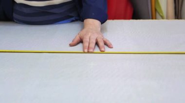 Karanlık bir kat büyük bir kadında ölçer ve gri malzeme kanepe için işaretler. Arkasındaki kadın malzemeleri farklı türleri vardır. O ölçme ve işaretleme malzeme kesim için hazırlanıyor.