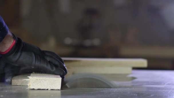在一家家具厂的一个年轻人附近剪掉木片作为沙发 家具生产过程 一个穿着深色外套的年轻人在切割机上为沙发剪断了木片 他戴着安全眼镜和手套 — 图库视频影像