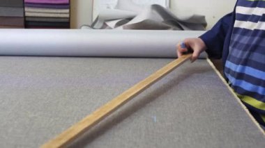 Karanlık bir kat büyük bir kadında ölçer ve gri malzeme kanepe için işaretler. Arkasındaki kadın malzemeleri farklı türleri vardır. O ölçme ve işaretleme malzeme kesim için hazırlanıyor.