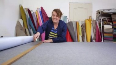 Karanlık bir kat büyük bir kadında ölçer ve gri malzeme bir takoz ile kanepe için işaretler. Arkasındaki kadın malzemeleri farklı türleri vardır. O ölçme ve işaretleme malzeme kesim için hazırlanıyor.