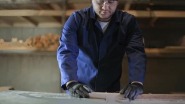 Genç ceket bir adam, bir karanlık kanepe için ahşap parçalar üzerinde kesme makinesi kesin. Bir duvar önünde araç ve Gereçleri bir yeri vardır. Koruyucu gözlük takıyor ve eldiven.