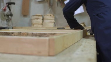 Genç ceket bir adam, bir karanlık birlikte çalışma masası üzerinde kanepe için ahşap parçaları koyar. Arkasında bir duvar üzerinde araç ve Gereçleri bir yeri vardır. Bir eldiven giyiyor.