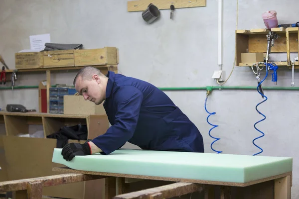 Joven en una fábrica de muebles aplica una espuma sobre un piec de madera — Foto de Stock