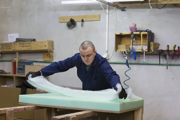 Jonge man in een meubelfabriek geldt een schuim op een houten stuk van de Bank — Stockfoto