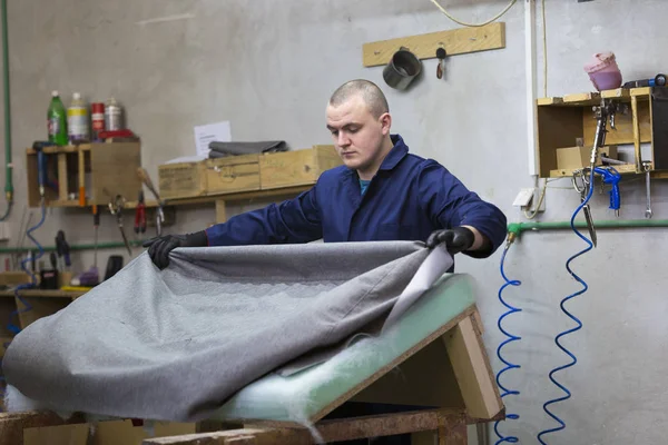 Молодой человек на мебельной фабрике, который кладет хлопок на одну часть дивана — стоковое фото