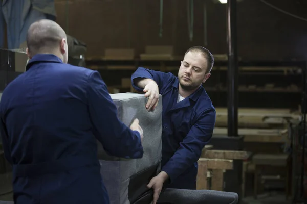 Two young men in a furniture factory put together one part of the sofa