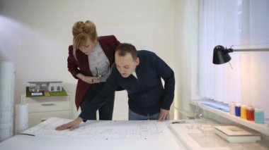 İki mimar, masada çalışan bir çıkman planına bakıyor. Onlar yorum ve bu konuda tartışıyorlar.