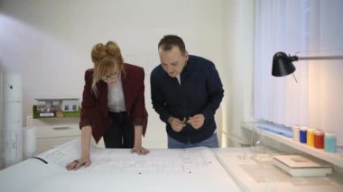 İki mimar, masada çalışan bir çıkman planına bakıyor. Onlar yorum ve bu konuda tartışıyorlar.