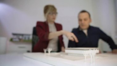 Ofiste iki mimar bir ev modeline bakarak masada oturuyor. Onlar döndürüyor ve tartışıyorlar. Gözlükler ile düşünceli tasarımcılar proje hakkında düşünme.