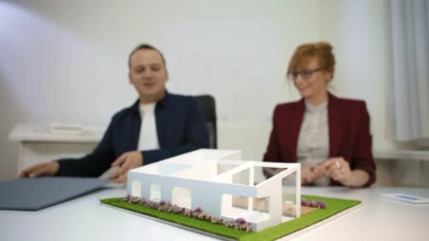 机の上で家のモデルと遊ぶオフィスの2人の建築家 屋根とプールを置いている — ストック動画
