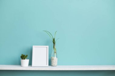 Resim çerçevesi mockup ile modern oda dekorasyonu. Su ve sulu örümcek bitki kesimleri ile pastel turkuaz duvara karşı beyaz raf.