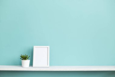 Resim çerçevesi mockup ile modern oda dekorasyonu. Saksı lı sulu bitki ile pastel turkuaz duvara karşı beyaz raf.