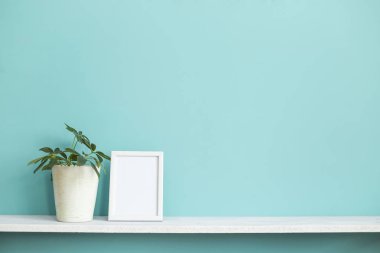 Resim çerçevesi mockup ile modern oda dekorasyonu. Saksı schefflera bitki ile pastel turkuaz duvara karşı beyaz raf.